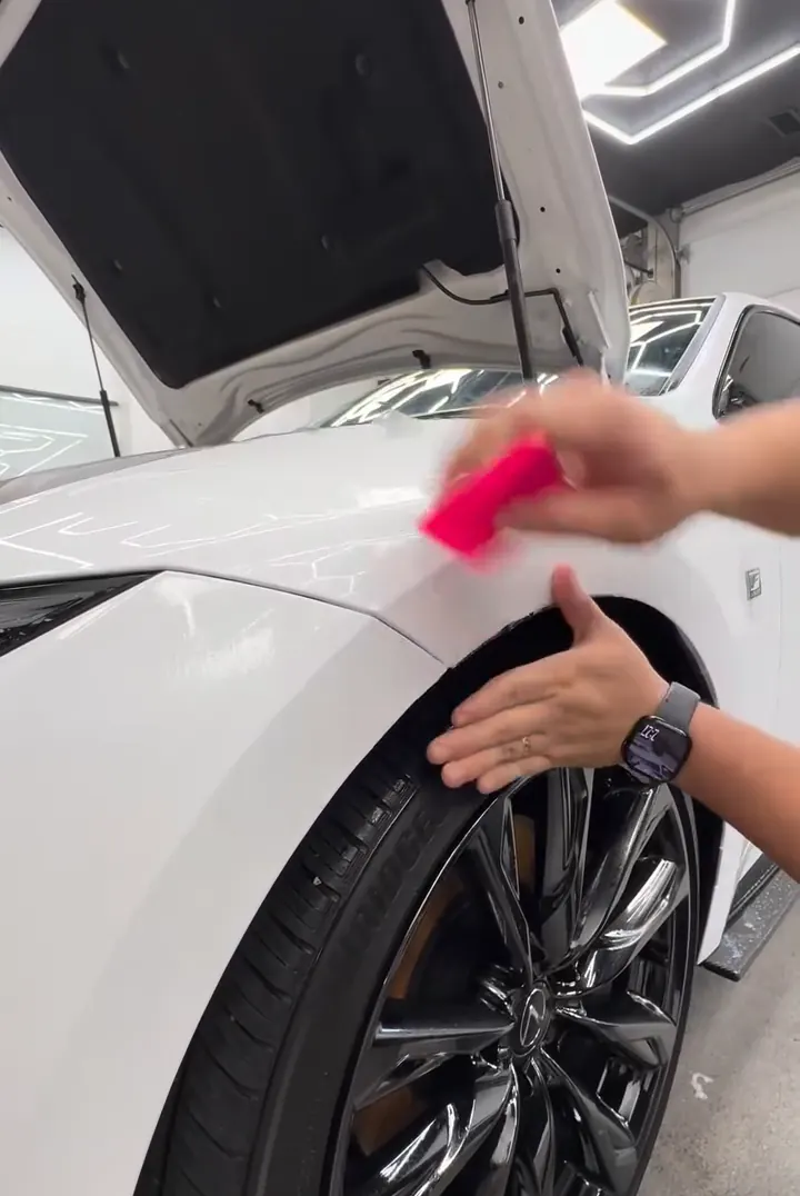 Installer squeegeeing XPEL film onto a white fender